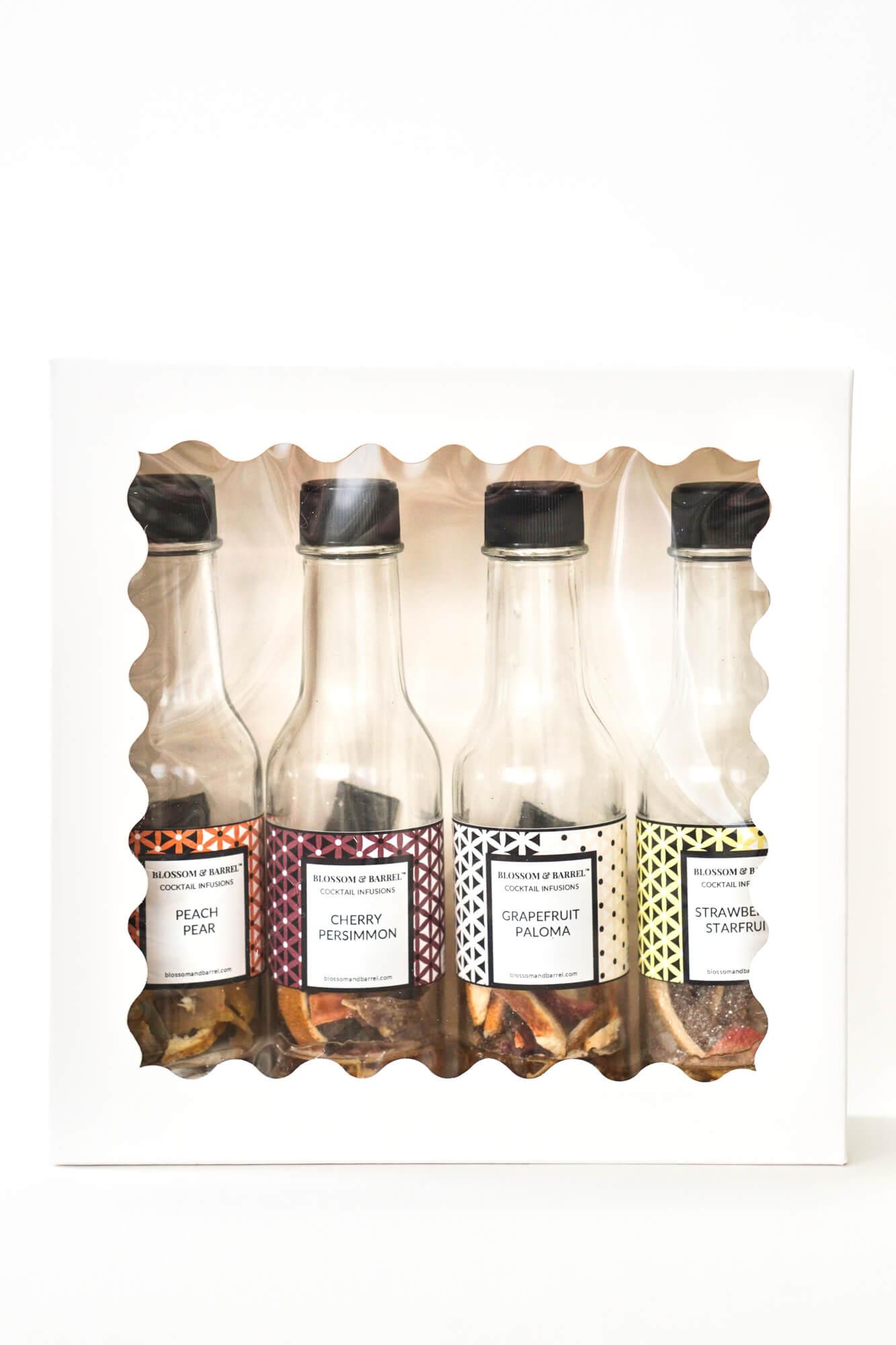 Set of four small cocktail infusion bottles with decorative labels in a white packaging tray.