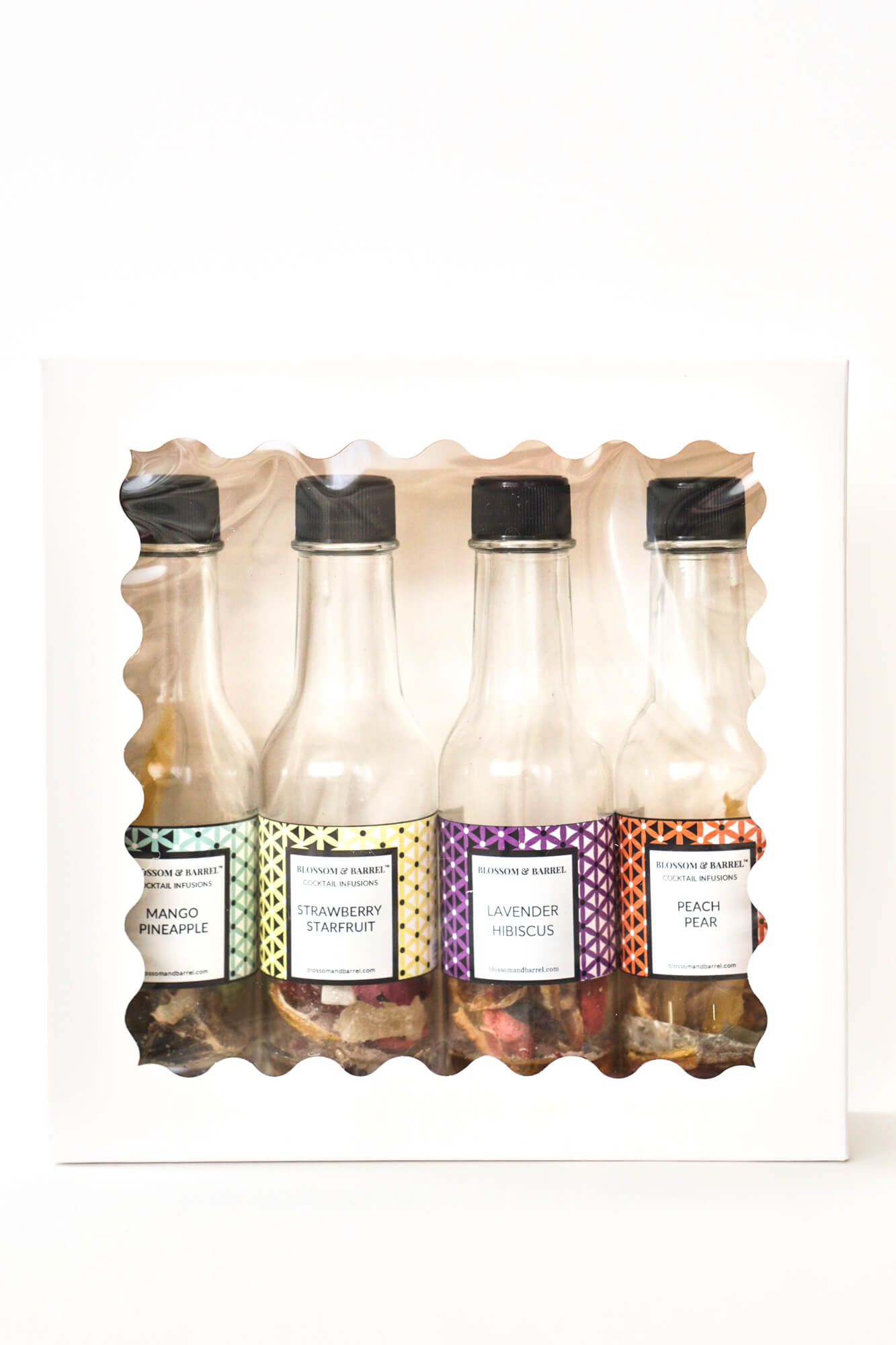 Pack of four small cocktail infusion bottles with colorful labels on a white background